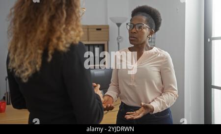 Two adult women engage in a serious conversation in an office interior, implying a business discussion or partnership between employees or colleagues Stock Photo