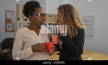 Women discussing business while holding coffee mugs in an office environment, highlighting collaboration and communication between colleagues Stock Photo