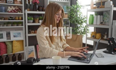 Young woman working on a laptop in a beautifully decorated home decor shop filled with stylish decorations and indoor plants, surrounded by attractive Stock Photo