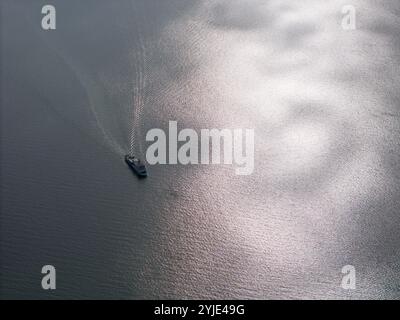 Small ferry boat moving on lake aerial drone view on bright day Stock Photo