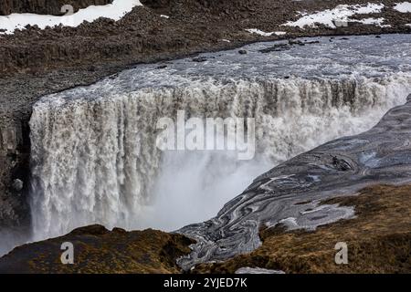 Dettifoss waterfall in Vatnajokull National Park in Northeast Iceland, waterfall view with basalt columns, ice and snow and water spray. Stock Photo