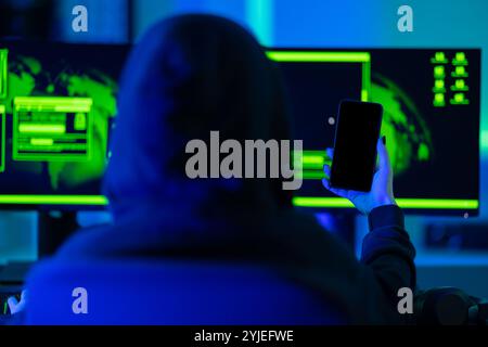 Hacker using smartphone in front of dual monitors with green glow Stock Photo