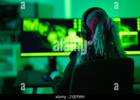 Female hacker working on cybersecurity tasks in a green lit room Stock Photo