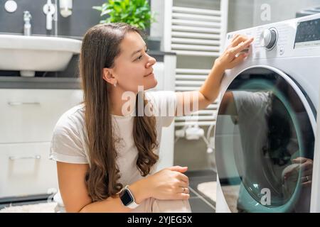 Young woman adjusting washing parameters on washing machine control panel in home bathroom Stock Photo