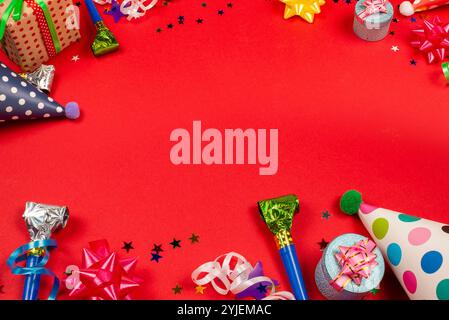 Festive golden and purple stars of confetti  and a present, birthday caps on a red background. Space for text or design. Stock Photo