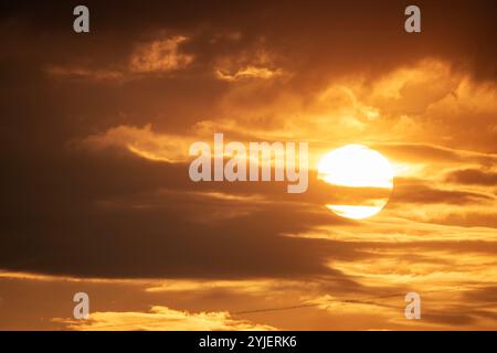 A dramatic view of the sun setting behind layers of clouds, casting a warm, golden light over the sky Stock Photo