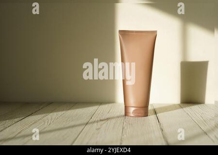 tan-colored tube stands on a rustic wooden surface, casting a soft shadow on the wall Stock Photo