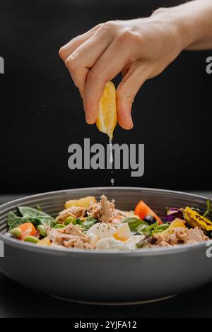 Fresh lemon juice squeezed over a nutritious tuna salad with poached egg, greens and vegetables Stock Photo