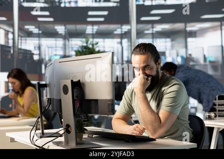 Company personnel sitting at desks in office, doing research for team project. Man looking at computer screen next to staff members in modern relaxed workplace solving tasks during job shift Stock Photo