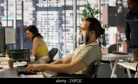 Person with impairment processing and analyzing data to automate decision making processes. IT specialist with disability programming in office, sitting in wheelchair, camera A Stock Photo