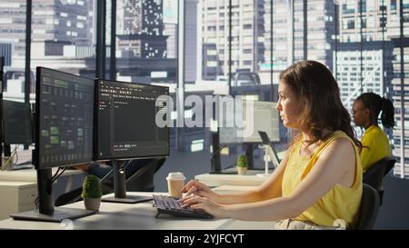 Manager in wheelchair passing by desk of employee testing machine learning company software to minimize occurrence of bugs. Woman works in inclusive workspace with workers with disabilities, camera B Stock Photo
