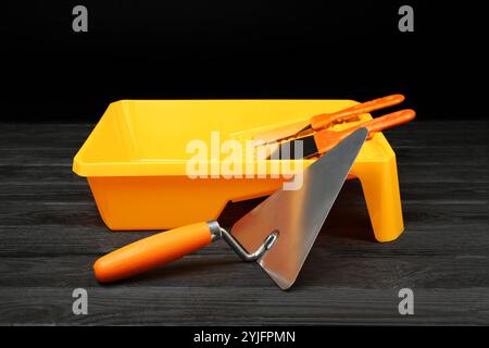 Tray and putty knives on dark wooden table. Construction tools Stock Photo