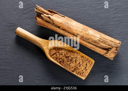 Closeup image of broken pieces of cinnamon sticks scattered on a dark gray slate surface. The cinnamon pieces are light brown, with rough textures and Stock Photo