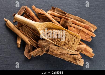 Closeup image of broken pieces of cinnamon sticks scattered on a dark gray slate surface. The cinnamon pieces are light brown, with rough textures and Stock Photo