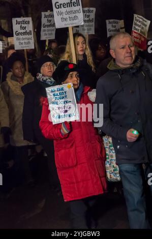 London, UK. 14th December 2017. A woman carries a placard 'In the Silent Night We Cry - Justice for Grenfell' on the monthly slow and silent walk to demand justice and remember those killed at Grenfell Tower on the 6 month anniversary of the tragic fire. The families of those who died and survivors made homeless by the fire marched at the front, together with local clergy. Many carried pictures of the victims and flowers, as well as green lights and green heart-shaped symbols. Placards and posters called for Justice for Grenfell, which many fear the official inquiry will fail to provide. I lef Stock Photo