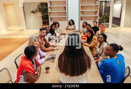 A businesswoman leads a dynamic discussion with a diverse group of professionals. The meeting takes place in a modern conference room, featuring colle Stock Photo