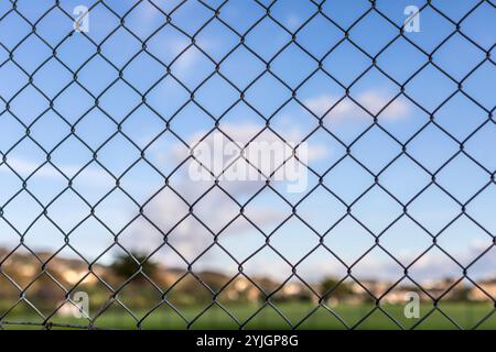 A chain link fence against a blue sky with clouds Stock Photo
