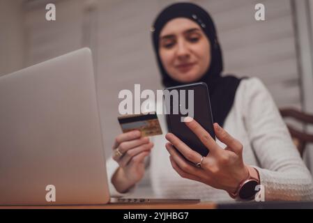 A young happy Muslim woman using mobile phone and holding credit card checking balance account or making money transfer. Online Payment Internet Stock Photo