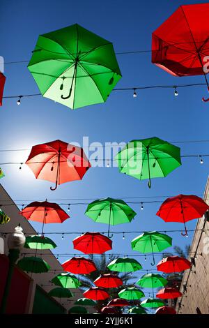 Red and green umbrellas hanging in the air against blue sky Stock Photo