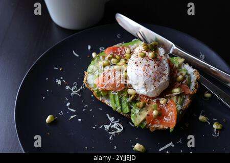 Poached eggs on top of smashed avocado on sourdough toast with smoked salmon and mung bean sprouts. Healthy breakfast with plate on table. Angel view. Stock Photo