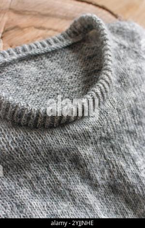 Gray cardigan sweater on wooden background, close up. Warm winter clothing. Rib sweater neck. Grey knitted sweater. Knitting pattern background. Stock Photo