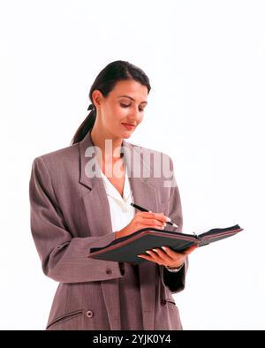 Business. Young executive woman indoors writing in organiser. Stock Photo