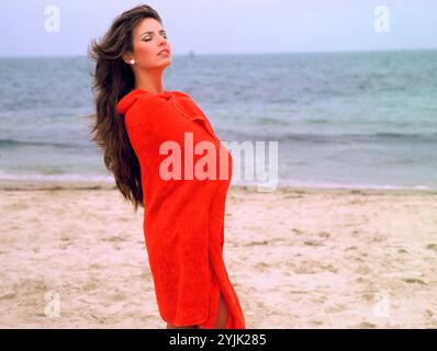 Young woman in red towel standing on the beach. Stock Photo