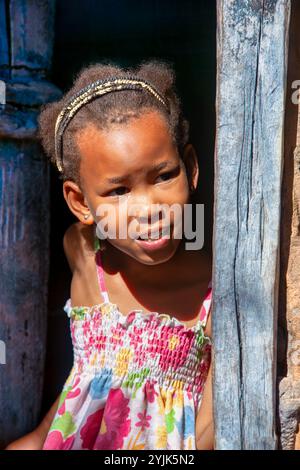 village african girl, curiosity peeping at the door, waiting for somebody, standing in front of her shack, mud house, in an informal settlement Stock Photo