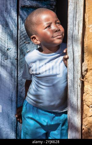 Single village african boy child standing in the frame of the wooden door, looking up visionary dreaming of a better future. Poverty in african villag Stock Photo