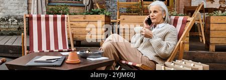 A beautiful mature woman relaxes in a casual chair, sipping coffee and engaged in conversation. Stock Photo