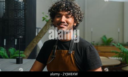 Happy joyful Latino American ethnic man male smiling cafe worker in apron guy waiter cleaner barista portrait small business owner employee looking at Stock Photo