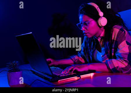 Portrait of young girl serious face play gaming laptop neon light dark room evening flat indoors Stock Photo