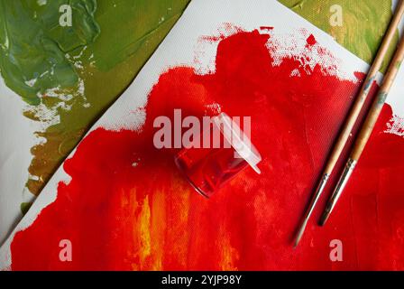 A photo featuring various canvases with acrylic paint layers, brushes, and a container for color. Stock Photo
