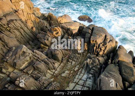 Goseong County, South Korea - November 3, 2024: Close-up view of the textured, layered rock formations at Neungpadae, with waves crashing against the Stock Photo