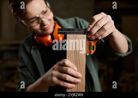 A skilled female carpenter focuses on accurate measurements while working on wood in her workshop. Stock Photo