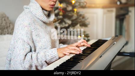 Closeup female's hands on the piano keys. Woman playing electric piano at home during Christmas holidays. Stock Photo