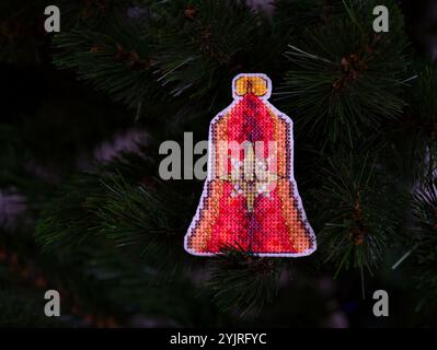 Red bell cross stitched Christmas ornament on Christmas tree. Stock Photo