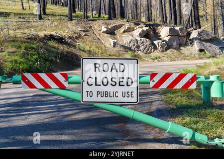 A road closed to public use sign in front of a gate, preventing access in the forest mountains. Stock Photo