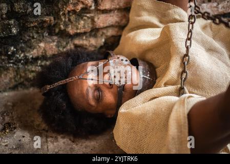 Portrait of a black woman chained and with an iron mask over her mouth lying on the floor. Slavery in Brazil. Representing the slave Anastacia. Stock Photo