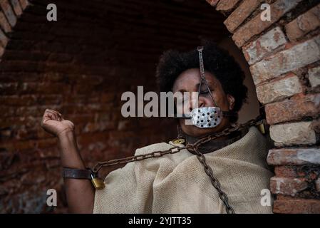 Portrait of a black woman dressed as a slave, chained with an iron mask over her mouth with her arm raised. Slavery in Brazil. Representation of the s Stock Photo