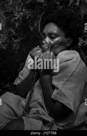 Black and white portrait of a woman dressed as a slave with an iron mask on her mouth and neck holding her hands. Slavery in Brazil. Representation of Stock Photo