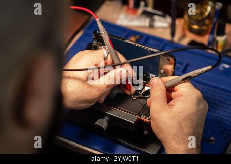 Technician repairing smartphone battery using soldering tools in a tech workshop during daylight hours Stock Photo