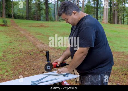 Craftsman is focused on using an angle grinder to cut through piece of metal while working outside Stock Photo