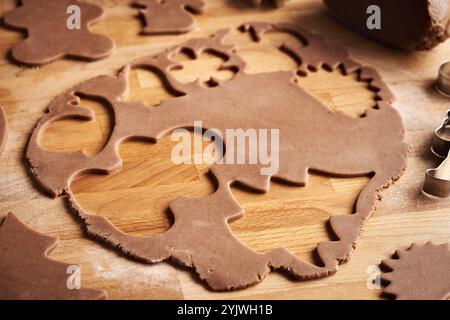 Cutting out shapes from rolled out raw pastry dough to prepare homemade gingerbread Christmas cookies Stock Photo