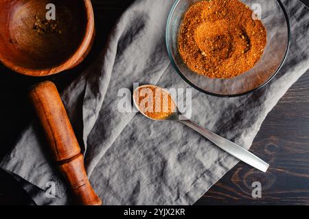 Spoonful of Homemade Berbere Spice Blend: Mixture of ground herbs and spices in a metal spoon next to a glass bowl and wooden mortar and pestle Stock Photo