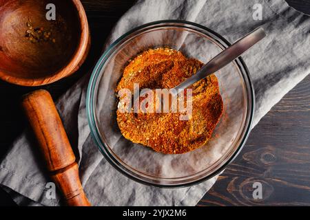 Mixing Spices to make Berbere Spice Blend: Ground herbs and spices mixed with a spoon in a glass bowl next to a wooden mortar and pestle Stock Photo