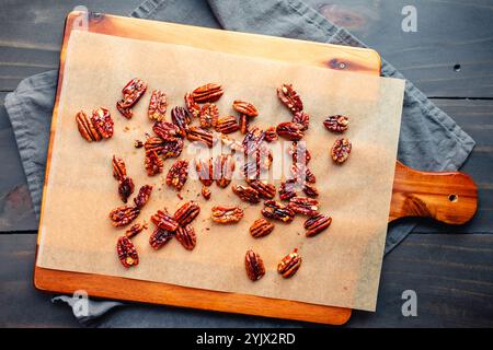 Sweet and Spicy Candied Pecans on Parchment Paper: Toasted pecans on unbleached baking paper lined wooden cutting board Stock Photo