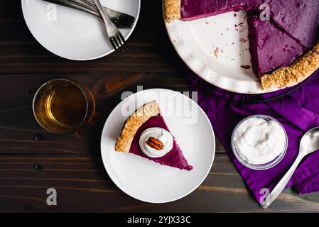 Slice of Purple Sweet Potato Pie Topped with Whipped Cream and a Pecan: Side view of a homemade purple sweet potato pie with a glass of bourbon Stock Photo