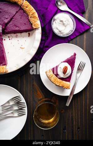 Slice of Purple Sweet Potato Pie Topped with Whipped Cream and a Pecan: Directly above a homemade purple sweet potato pie with a glass of bourbon Stock Photo
