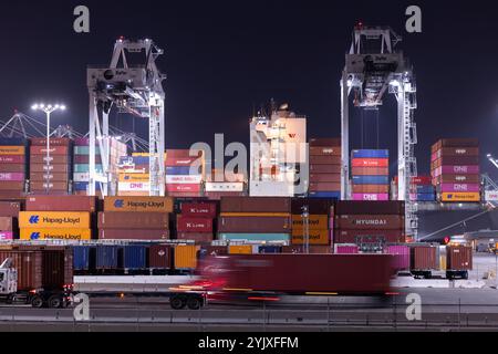 Wilmington, California, USA - July 16, 2021: Cranes unload intermodal containers from a ship at the port of Los Angeles, while semi trucks transport t Stock Photo